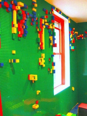 Quarto infantil com base de lego verde na parede, em que criança pode montar peças